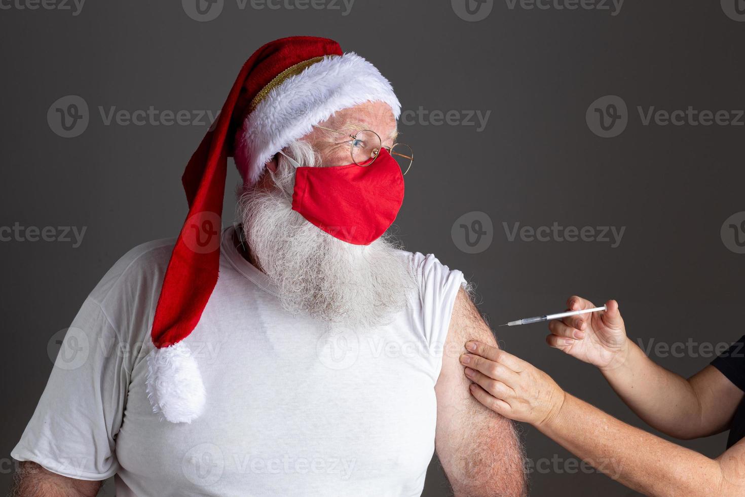 babbo natale che indossa una maschera per il viso che viene vaccinato con l'iniezione foto