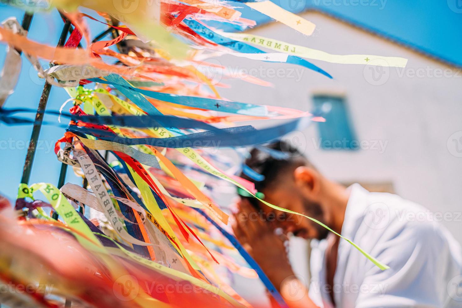 uomo latinoamericano che effettua un ordine con nastri brasiliani sul recinto di una chiesa ad arraial d'ajuda, bahia, brasile. concentrarsi su nastri colorati foto