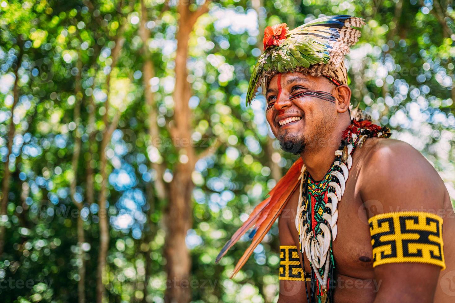 capo della tribù pataxo sorridente. indiano brasiliano con copricapo di piume e collana che guarda a sinistra foto