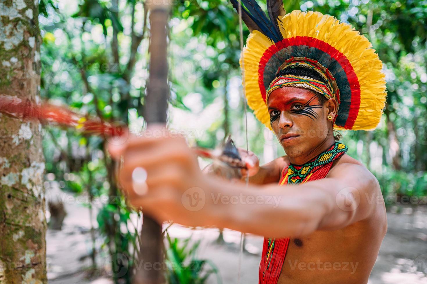 indiano della tribù pataxo usando arco e frecce. indiano brasiliano con copricapo di piume e collana foto