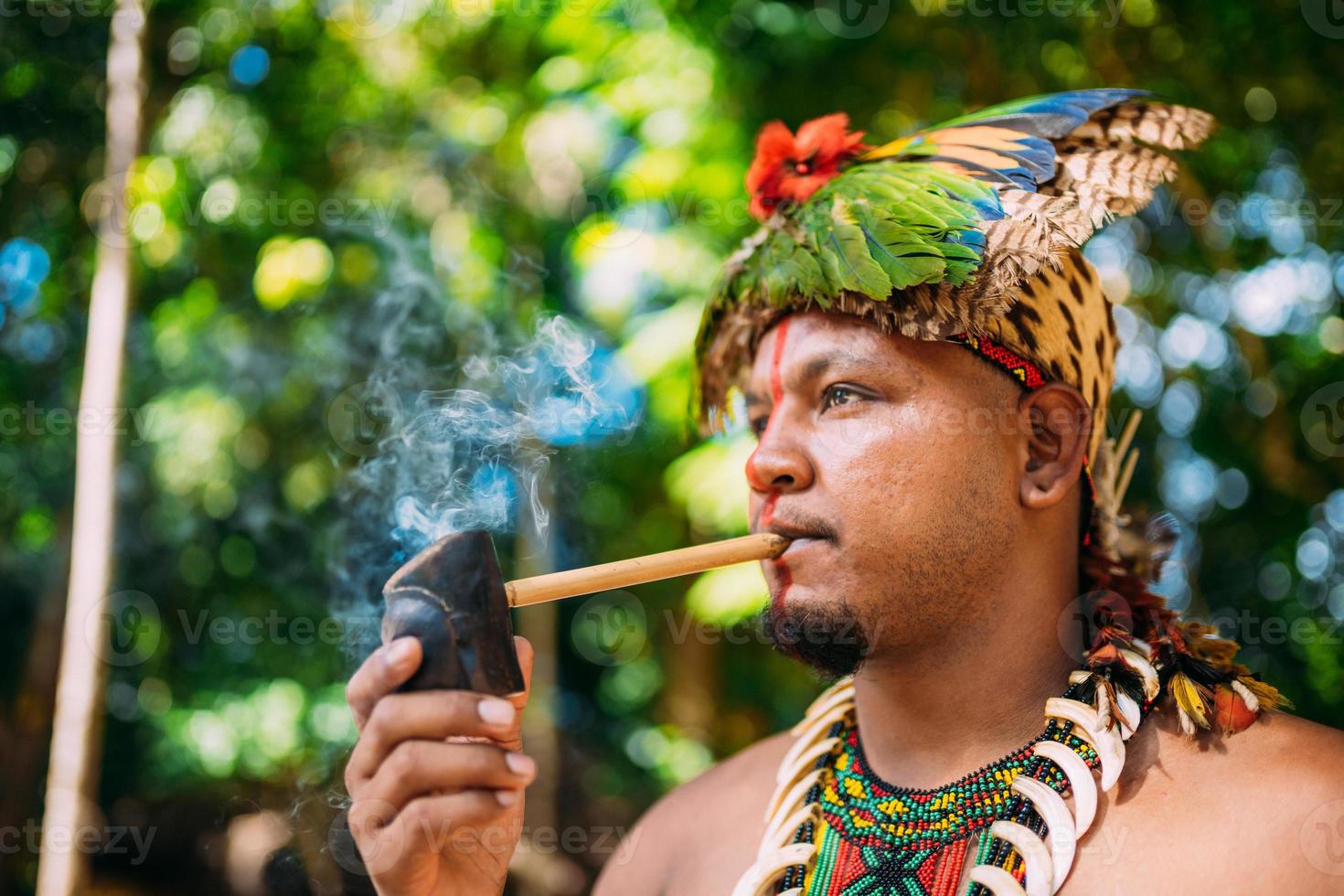 capo indiano della tribù pataxo che fuma la pipa . indiano brasiliano con copricapo di piume e collana foto