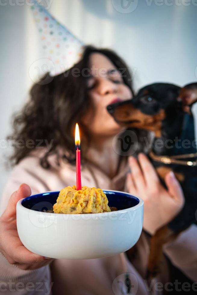 ragazza felice che dà una torta fatta in casa al suo cane, al chiuso foto