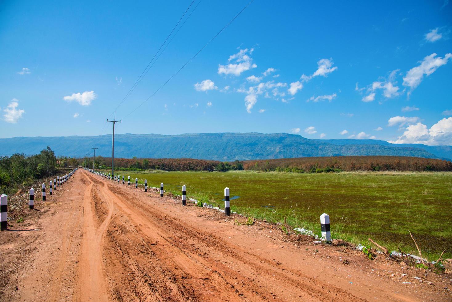 la ghiaia della strada sterrata nella campagna agricola va sullo sfondo del cielo azzurro della montagna foto