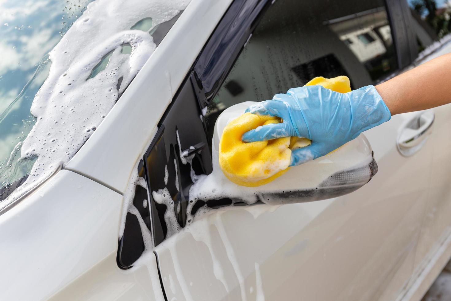 mano della donna che indossa guanti blu con spugna gialla per il lavaggio dello specchietto laterale dell'auto moderna o per la pulizia dell'automobile. concetto di autolavaggio foto