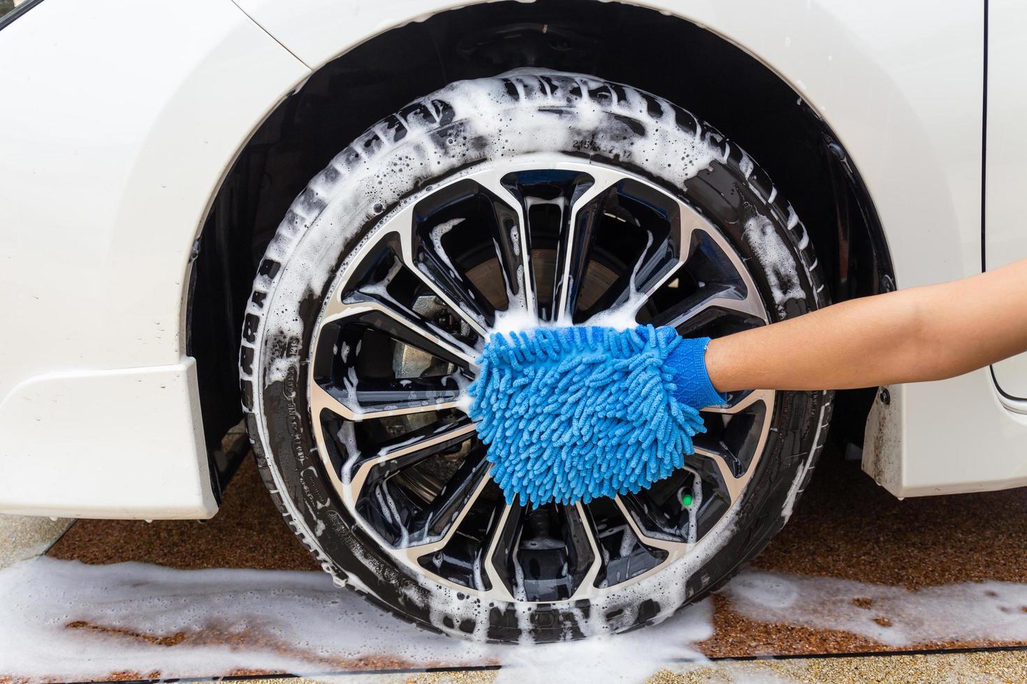 mano donna con tessuto in microfibra blu lavaggio ruota auto moderna o pulizia automobile. concetto di autolavaggio foto