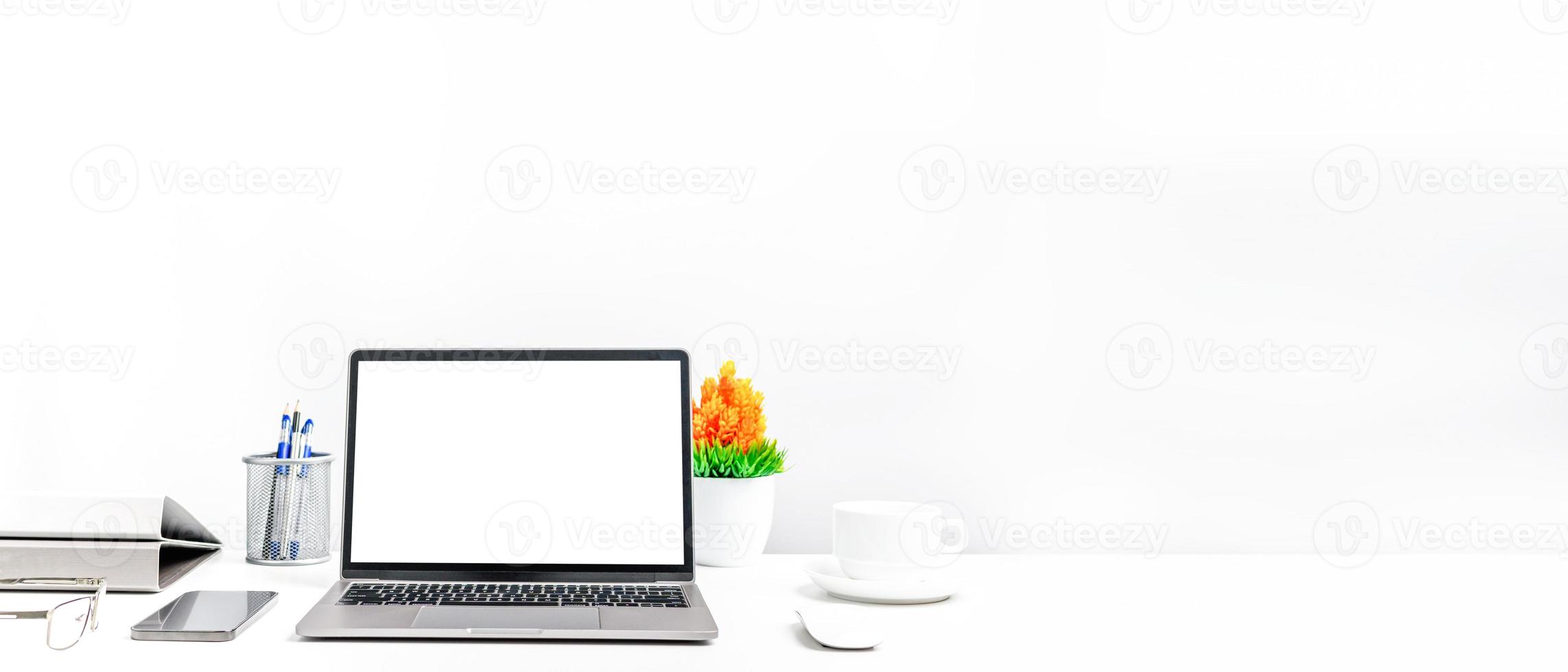 un laptop è uno schermo bianco vuoto su un tavolo in un ufficio. concetto di lavoro utilizzando smartphone tecnologici, notebook, tazza di caffè. copia spazio a destra per design o testo, primo piano, grigio e sfocatura dello sfondo foto