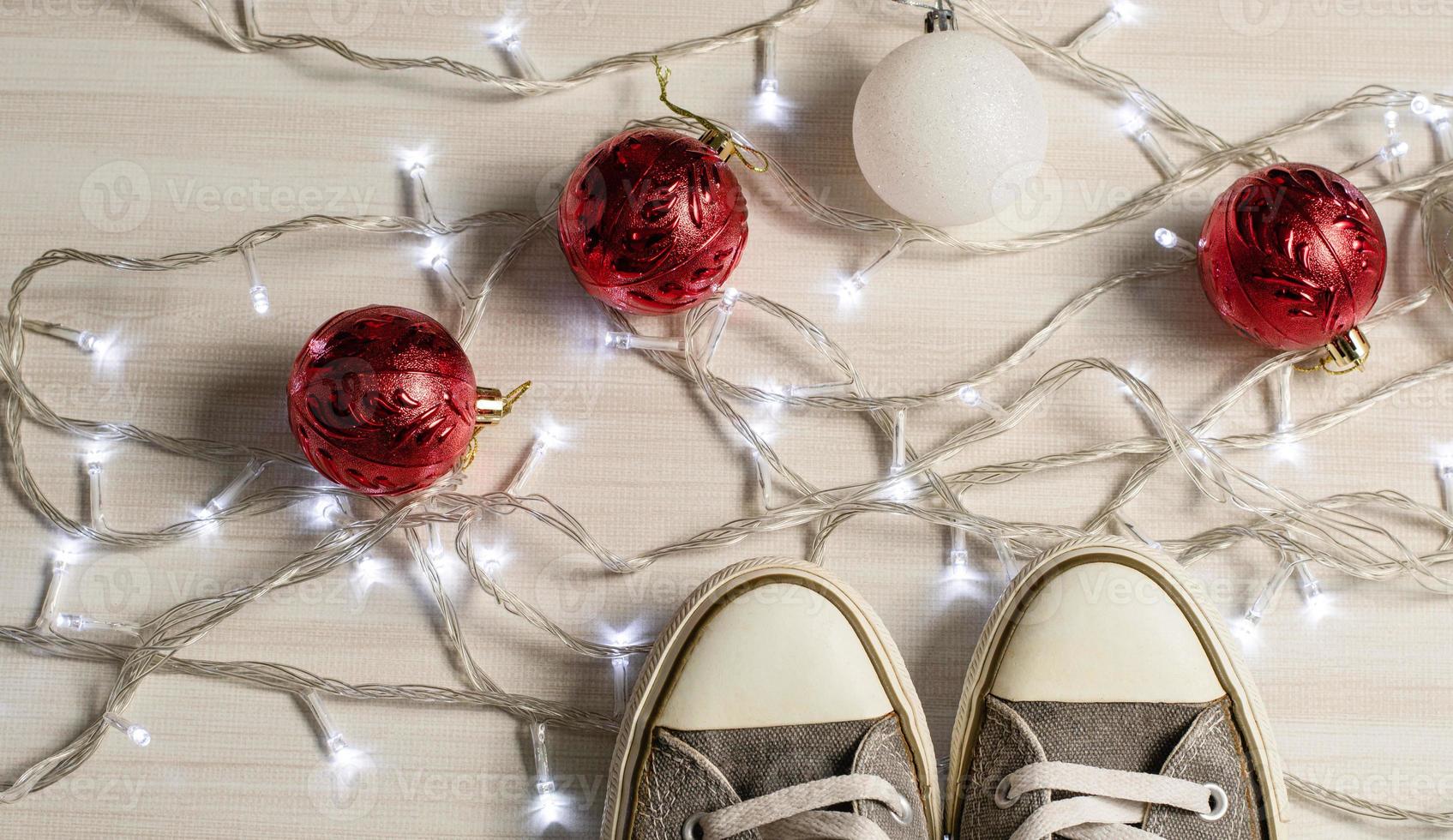 scarpe di tela poste su un tavolo di legno in soggiorno. concetto per la stagione natalizia, palla rossa e bianca, luci, luminose, scarpe da ginnastica. avvicinamento foto