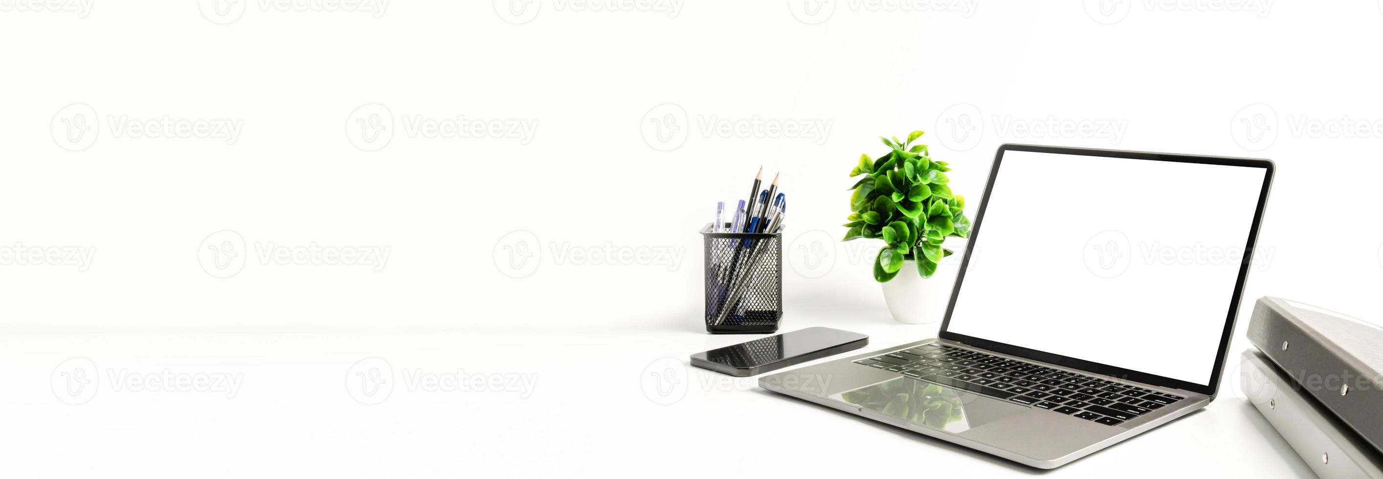 computer portatile con schermo bianco vuoto su un tavolo bianco in ufficio. concetto di lavoro utilizzando smartphone tecnologici, notebook, internet. copia spazio a sinistra per design o testo, primo piano, grigio e sfondo sfocato foto