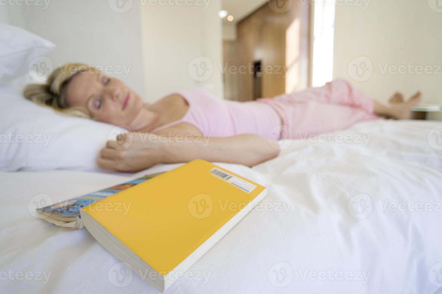 donna sdraiata sul letto addormentato, libro in primo piano foto