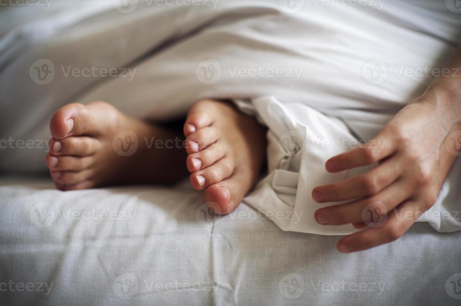 piedi del bambino addormentato e mano sulla biancheria da letto bianca foto