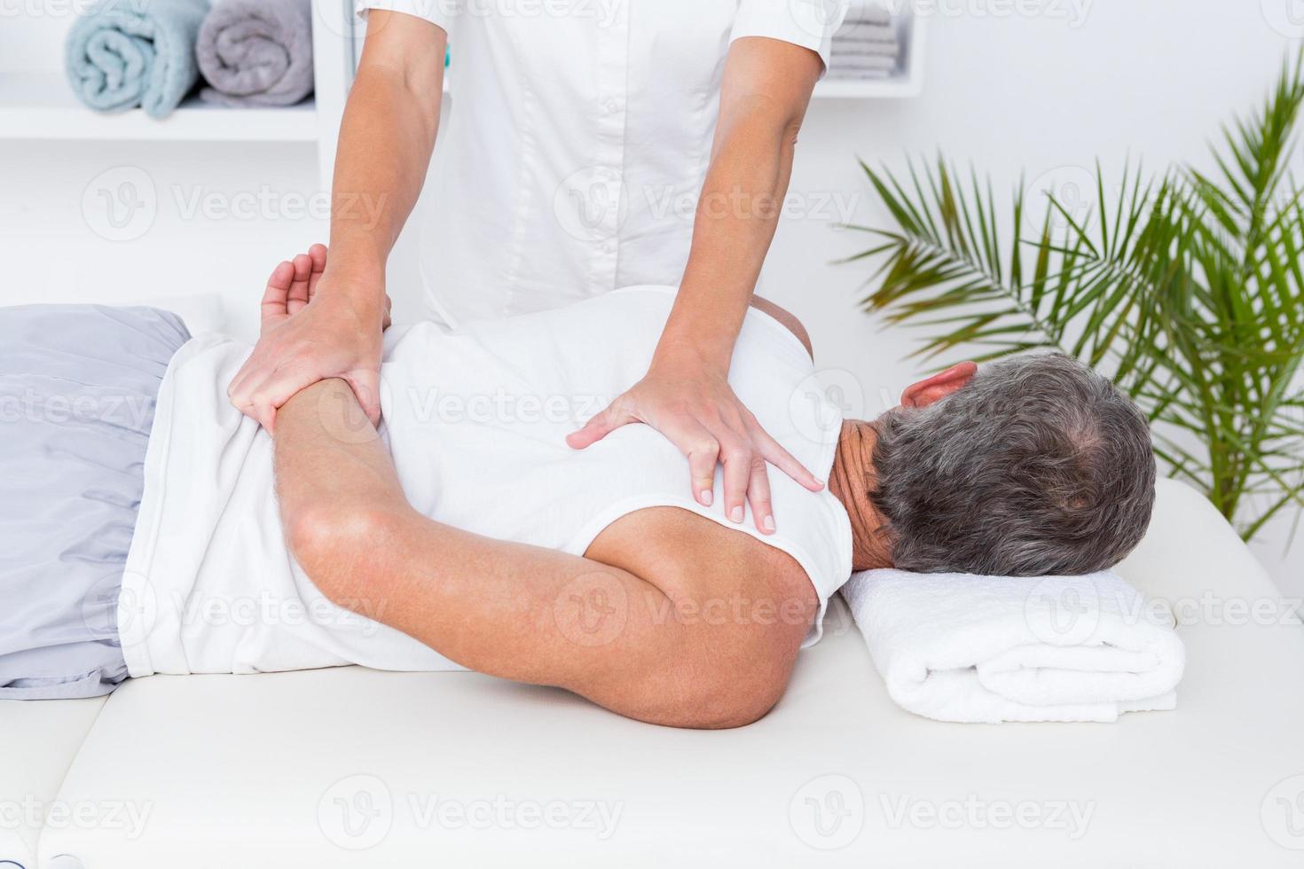 Fisioterapista che fa massaggio alla spalla al suo paziente foto