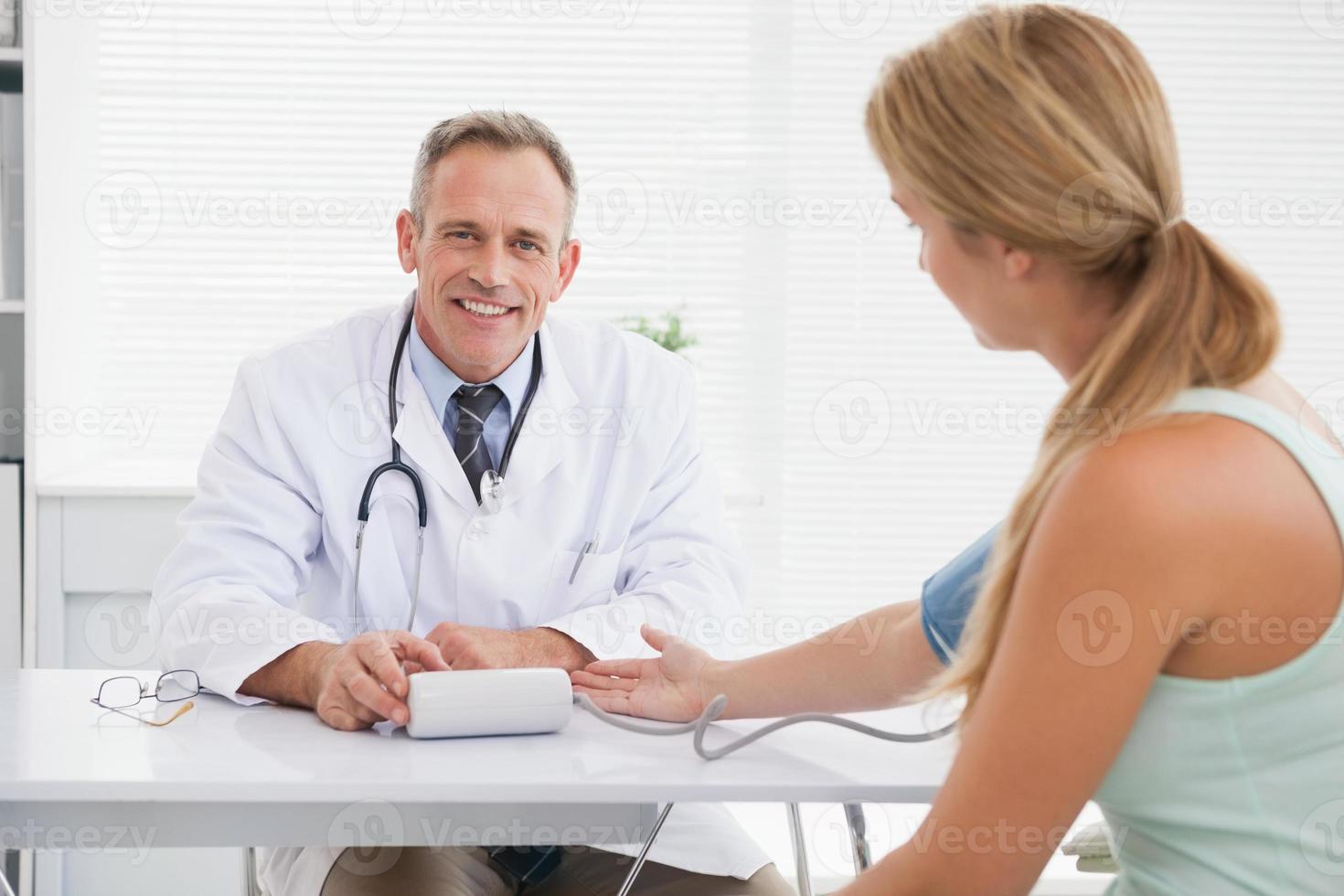 medico sorridente che cattura ai pazienti la pressione sanguigna foto