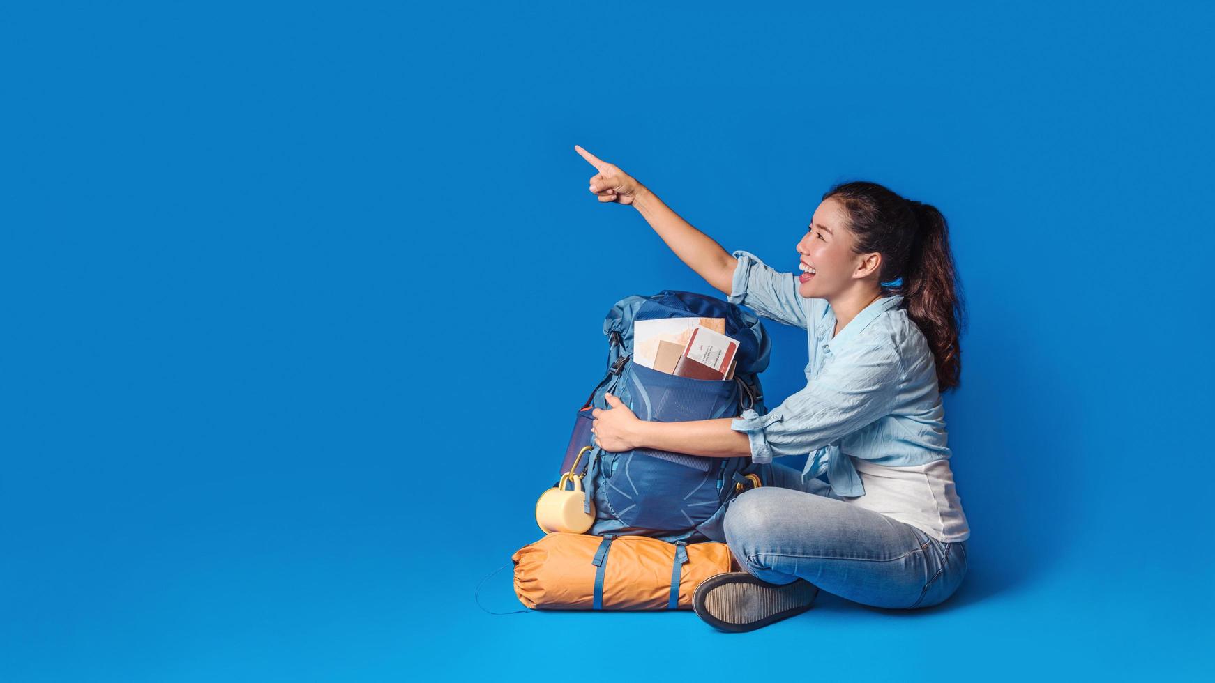 giovane viaggiatore asiatico donna felice in camicia blu con zaino con e attrezzatura per le vacanze dei viaggiatori con una mappa, su sfondo di colore blu. zaino da viaggio foto