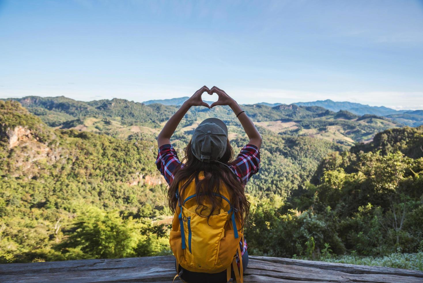 giovane turista con zaini felici di viaggiare ha alzato la mano per fare una forma a cuore e godersi lo scenario naturale sulla montagna. foto