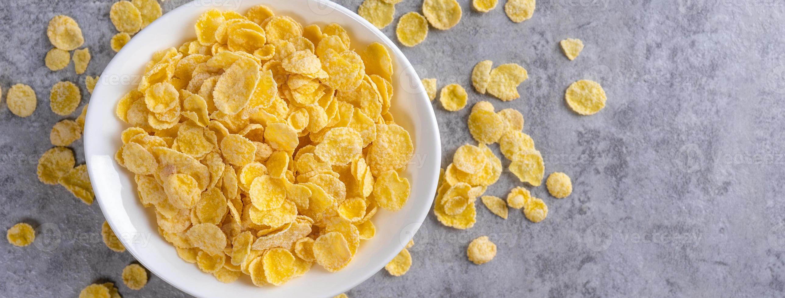 Ciotola di fiocchi di mais dolci su sfondo grigio di cemento, design piatto con vista dall'alto, concetto di colazione fresca e sana. foto