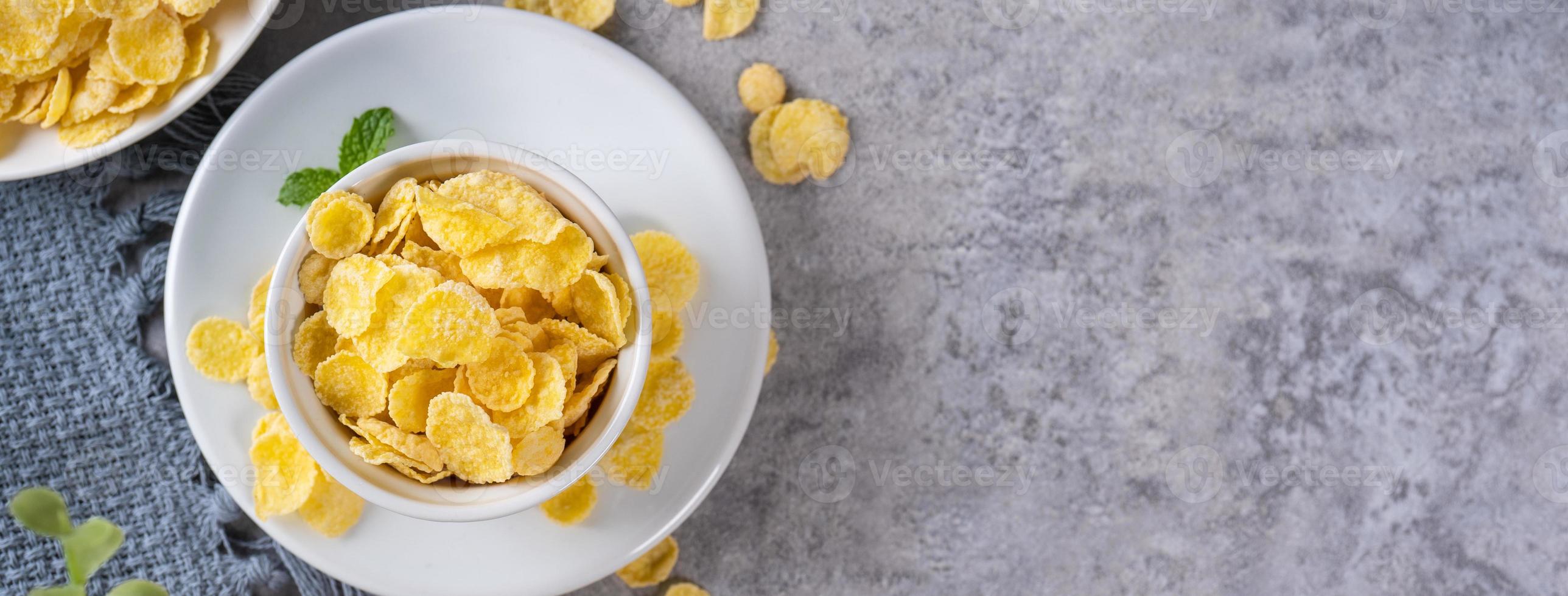 Ciotola di fiocchi di mais dolci su sfondo grigio di cemento, design piatto con vista dall'alto, concetto di colazione fresca e sana. foto