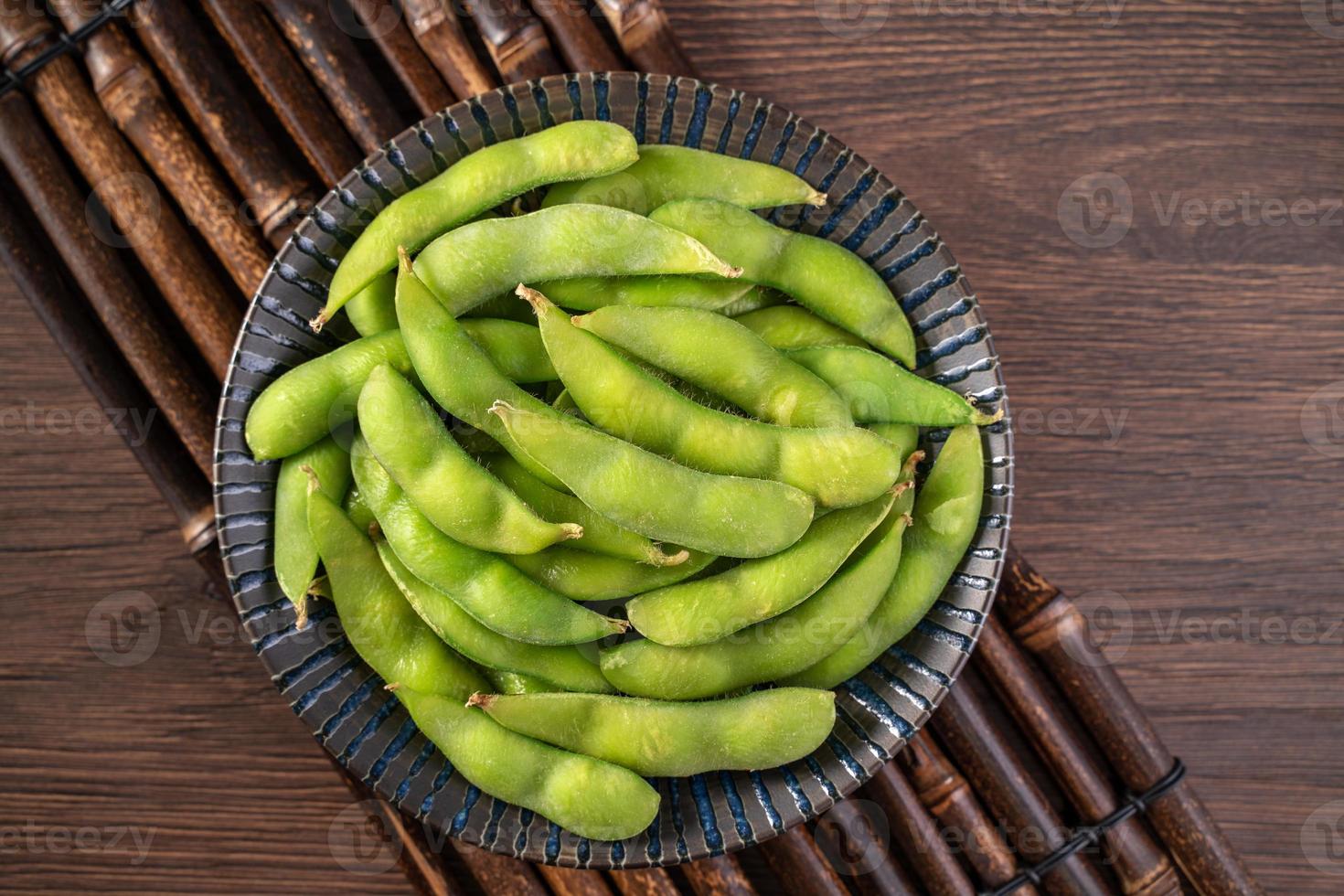 edamame bollito fresco cotto in un piatto sul vassoio di legno e sullo sfondo del tavolo, concetto di cibo proteico sano. foto