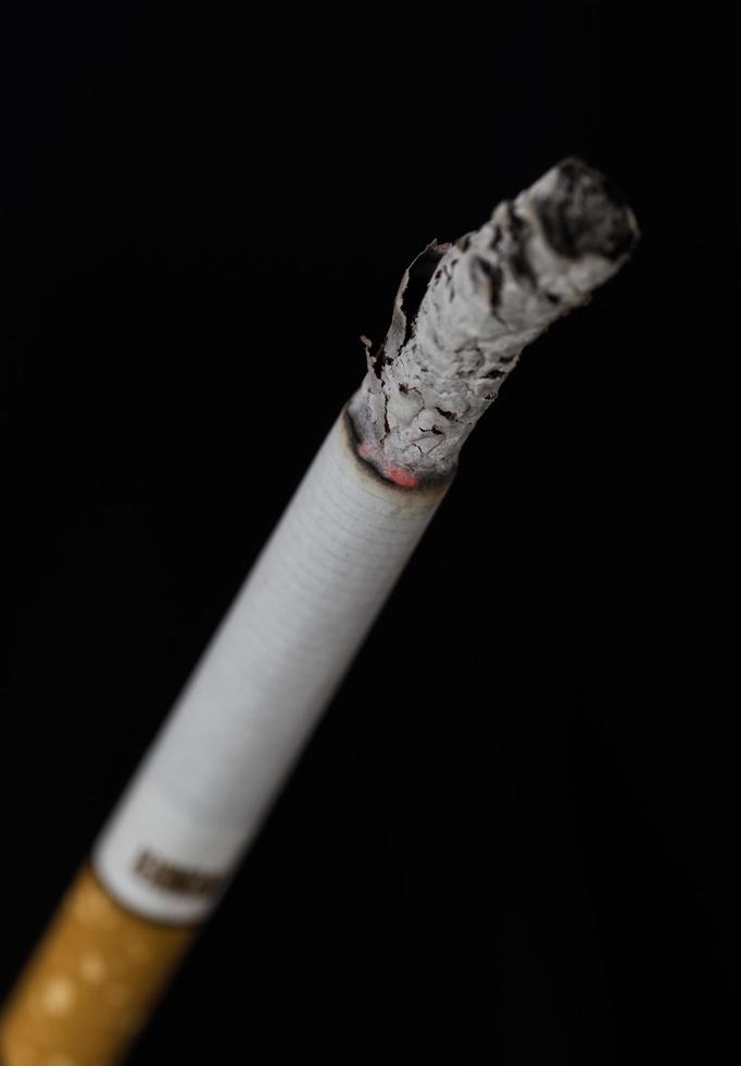 sigaretta accesa con fumo su sfondo nero foto