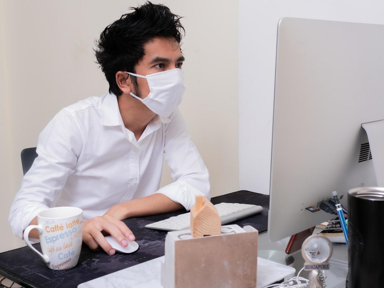 giovane ragazzo asiatico che indossa una maschera facciale che lavora su un computer portatile durante la pandemia di coronavirus foto
