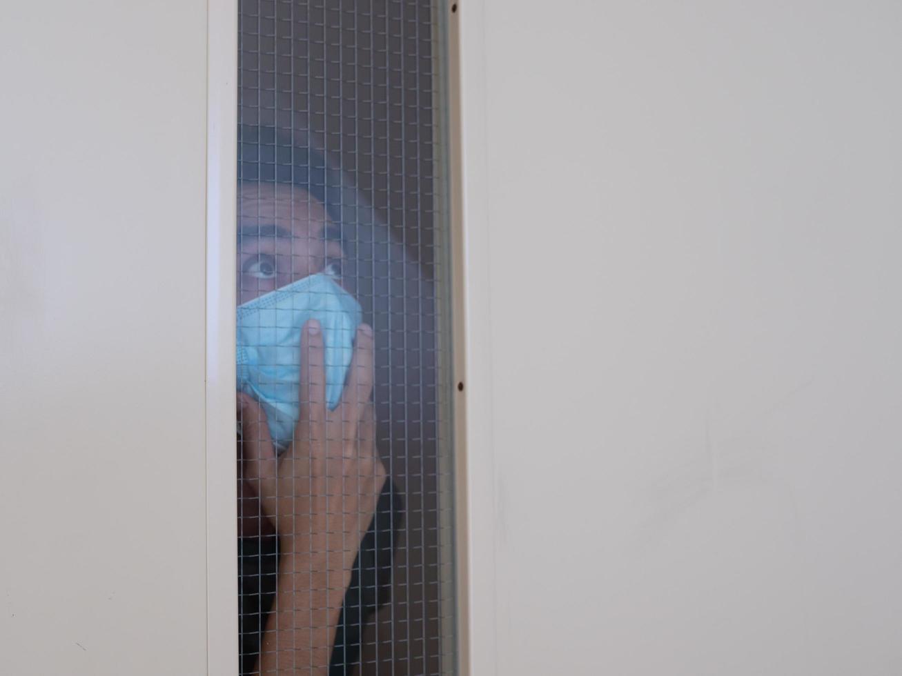 uomo solo in maschera medica che guarda attraverso la finestra. isolamento domiciliare per auto quarantena. concetto di quarantena domestica, prevenzione covid-19. situazione dell'epidemia di coronavirus foto