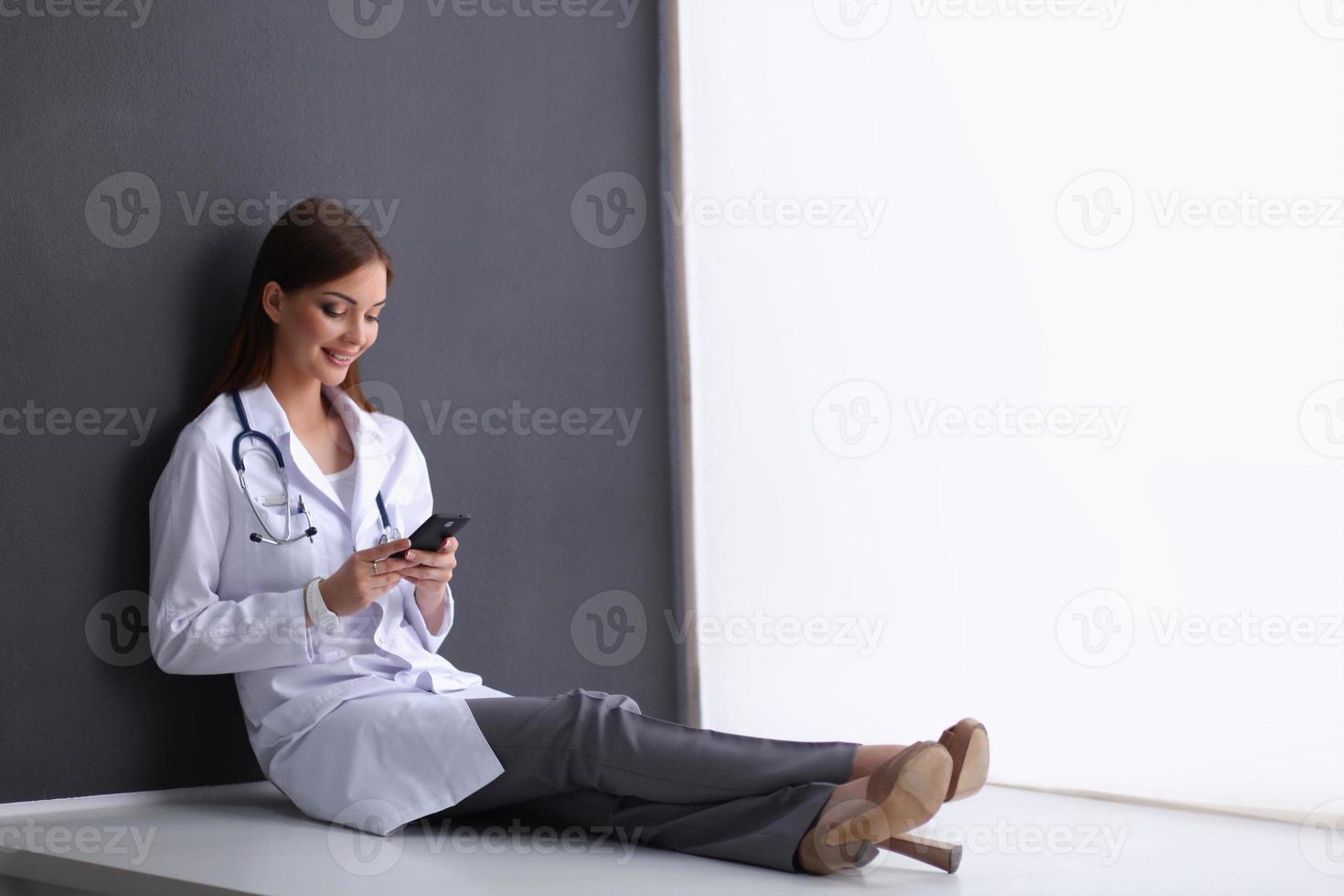 giovane donna dottore seduto sul pavimento con il telefono foto