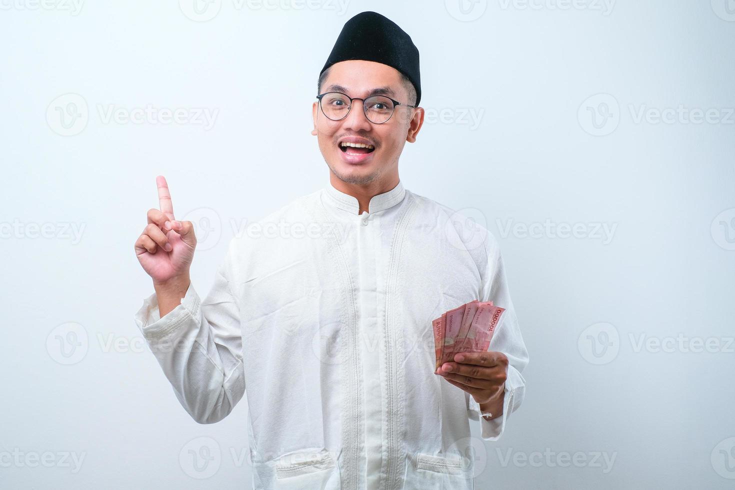 uomo musulmano asiatico che tiene la carta moneta rupia mentre punta il dito verso l'alto e sorride foto