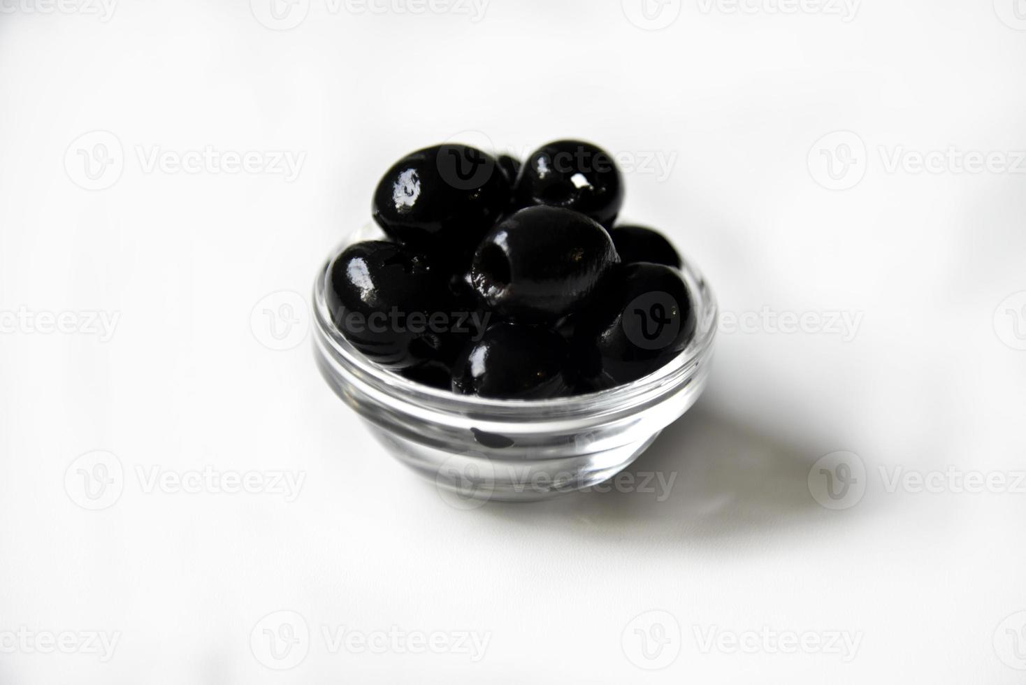olive nere in una casseruola bianca e di vetro su fondo bianco. foto