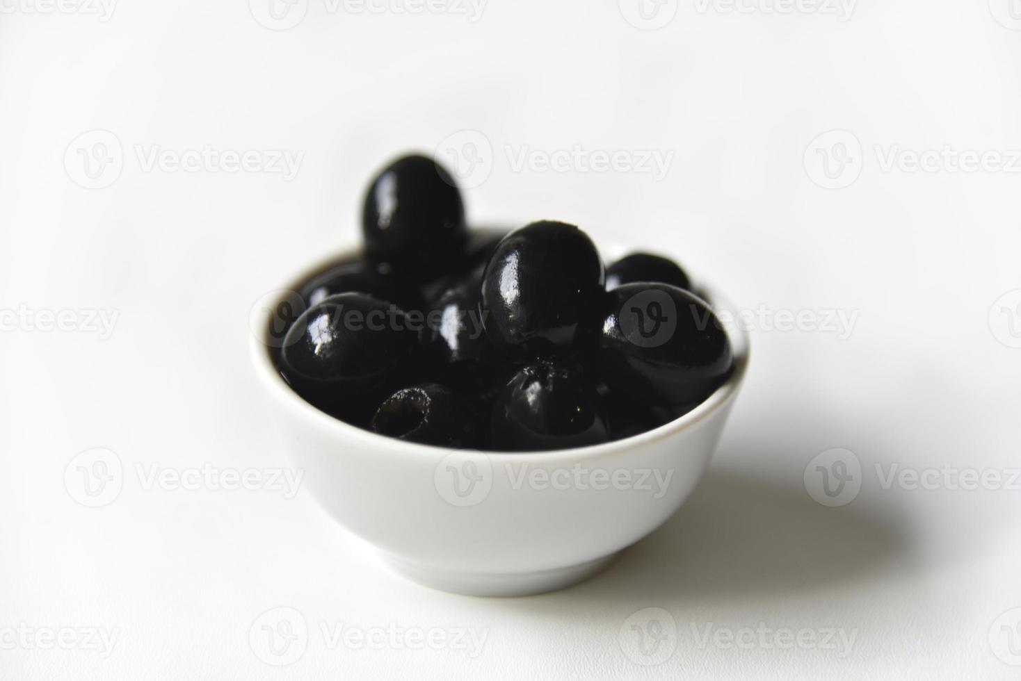 olive nere in una casseruola bianca e di vetro su fondo bianco. foto