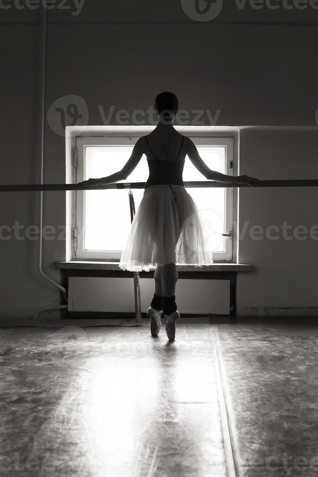 un'affascinante ballerina in body posa elementi di balletto in un copricapo in uno studio fotografico foto