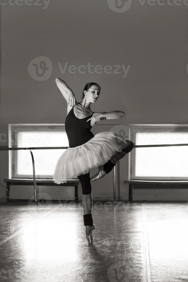 un'affascinante ballerina in body posa elementi di balletto in un copricapo in uno studio fotografico foto