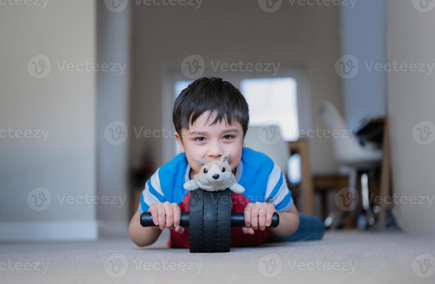 ragazzo felice sdraiato sul pavimento che gioca a rotelle con il giocattolo del cane, bambino con la faccia sorridente che gioca da solo a casa nel fine settimana, bambino positivo che si rilassa a casa al mattino foto