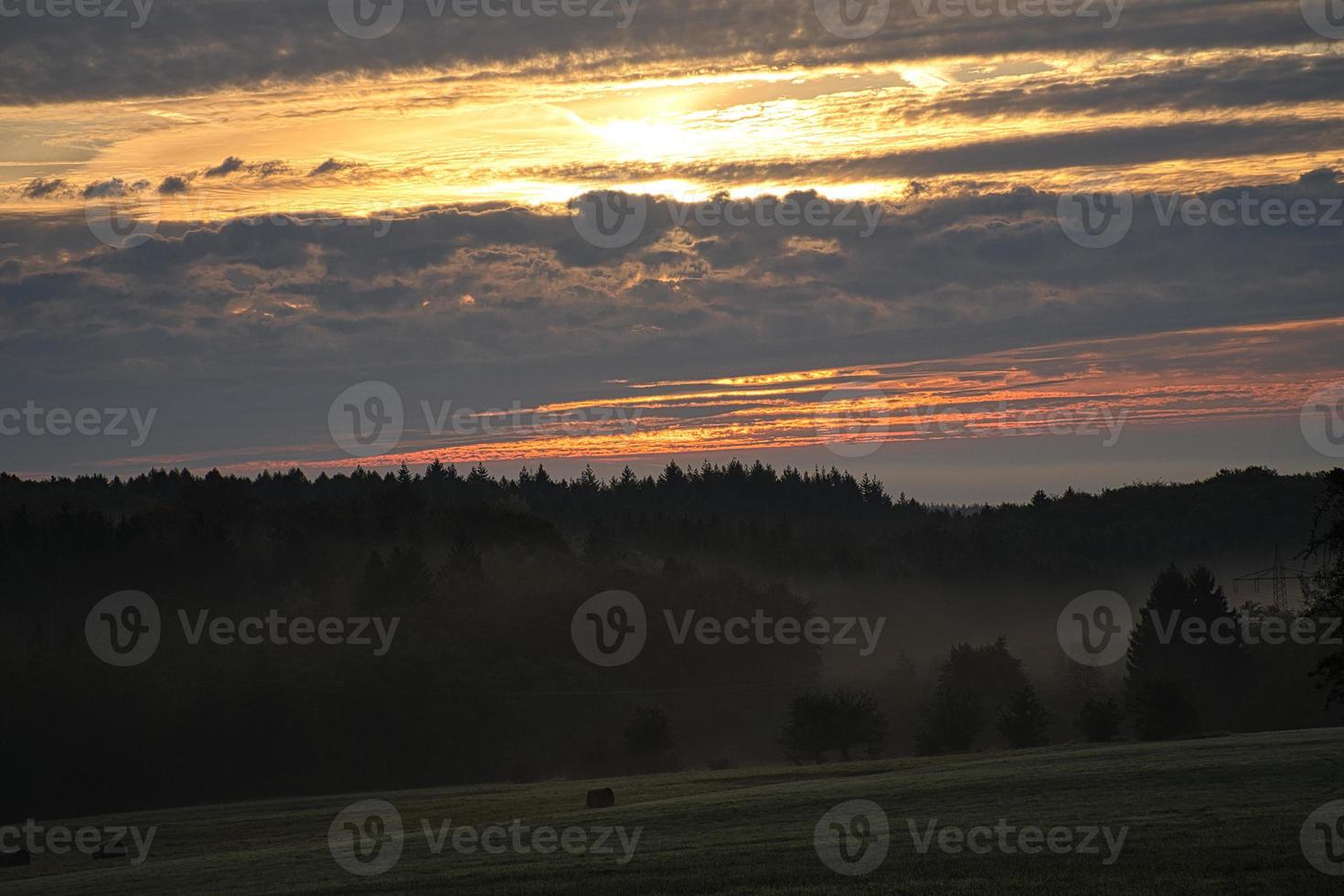 sole che sorge sul prato nebbioso al mattino nel saarland. il cielo sembra bruciare foto