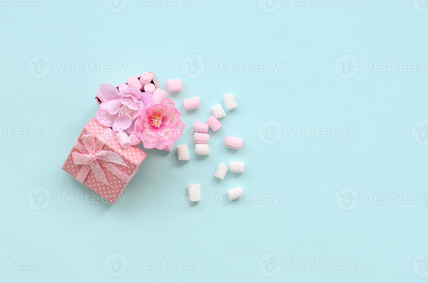 confezione regalo rosa fiorita cosparsa di marshmallow su sfondo blu foto