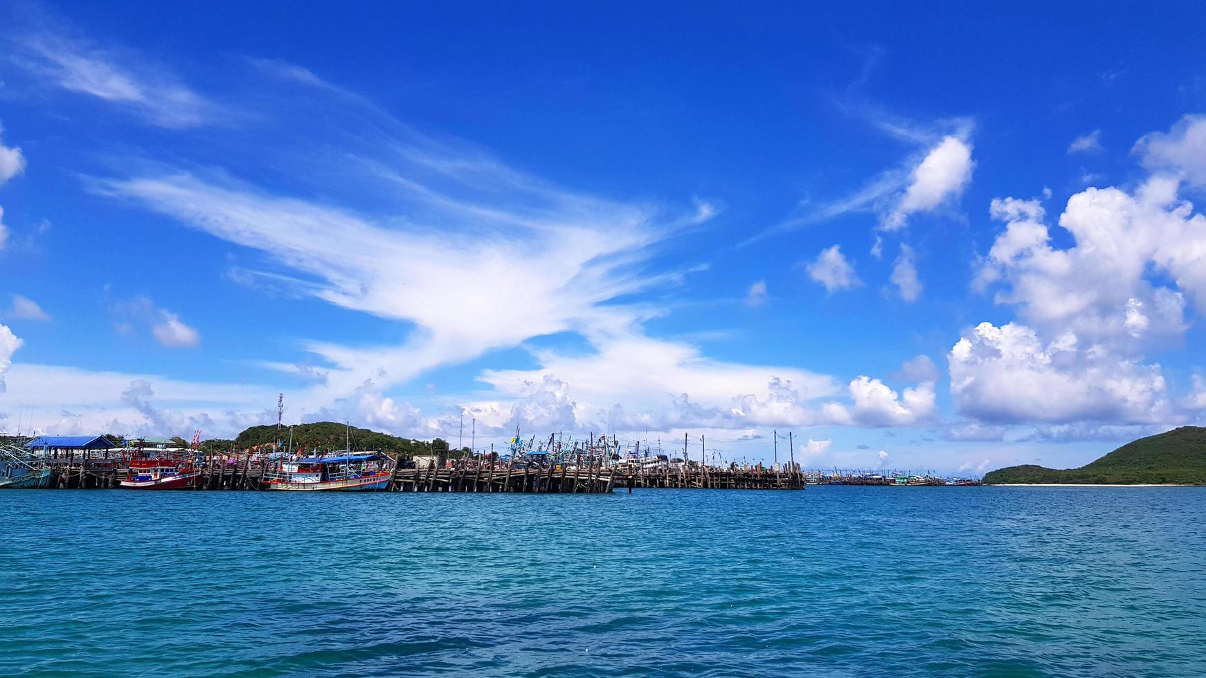 molti pescherecci parcheggiati sul mare al porto vicino alla costa e alla comunità con cielo blu, nuvole bianche e sfondo verde della montagna e spazio per la copia. paesaggio dell'oceano o del mare. bella vista e natura foto