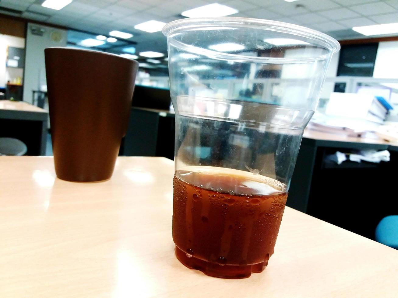 bicchiere di plastica di caffè nero e vetro marrone con sfondo sfocato dell'ufficio. bibita rinfrescante e acqua. foto