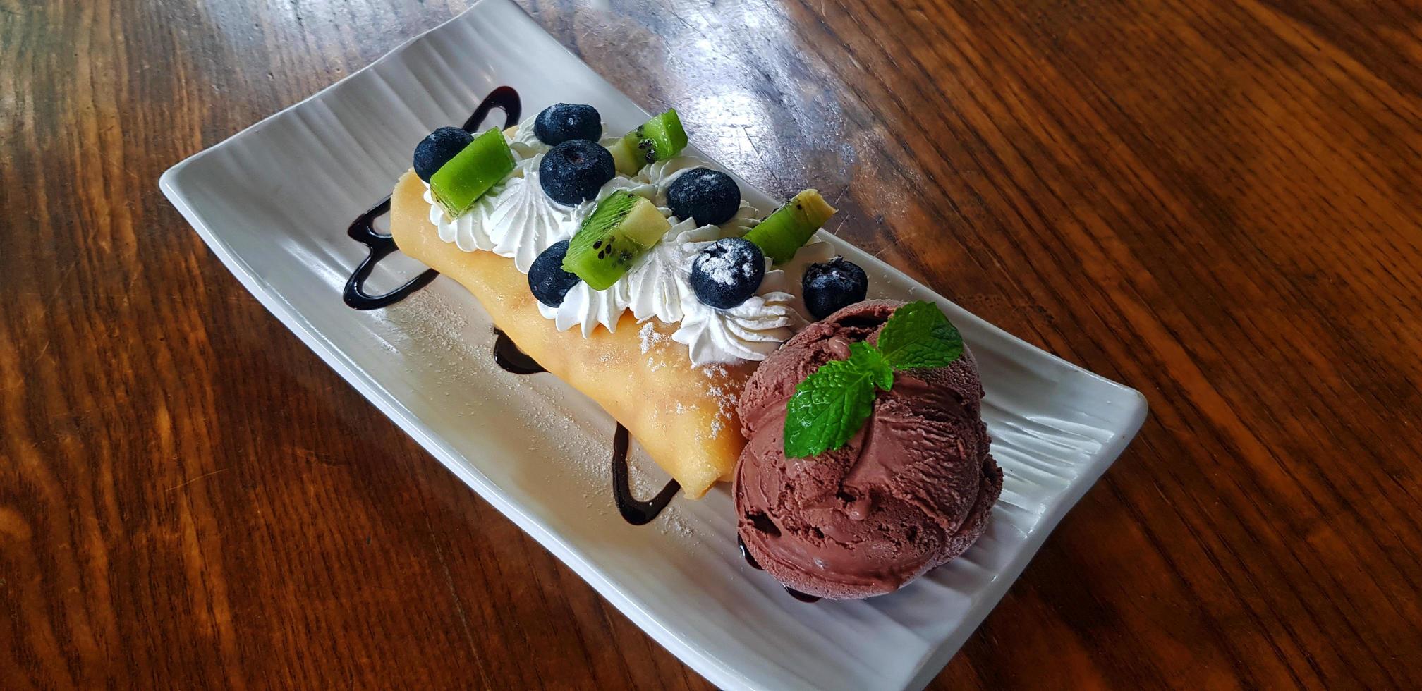 vista dall'alto del gelato al cioccolato con kiwi fresco a fette, frutti di bosco o lampone e panna montata in un piatto o piatto su un tavolo di legno con spazio per la copia al bar. piatto di cibo da dessert con frutta fresca. foto