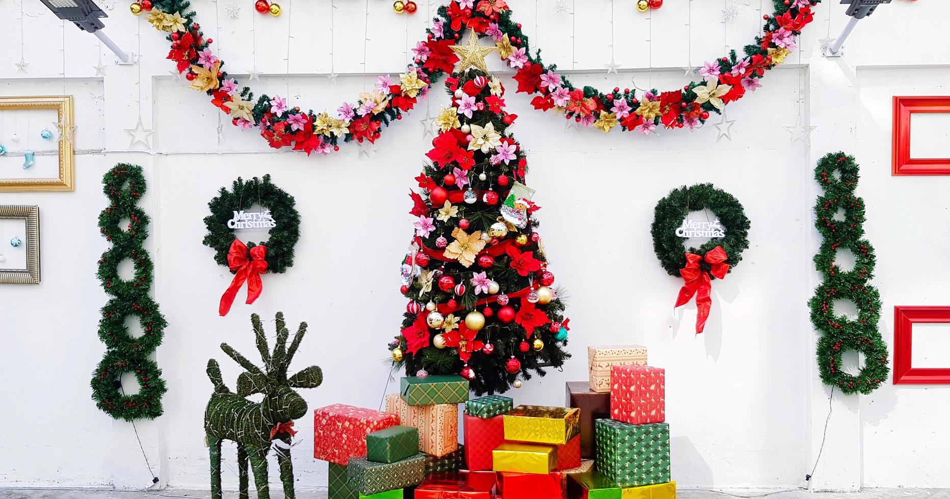 albero di pino decorato concetto di buon natale con palla, regalo, fiore, nastro e stella con sfondo bianco muro e ghirlanda di foglie verdi. foto