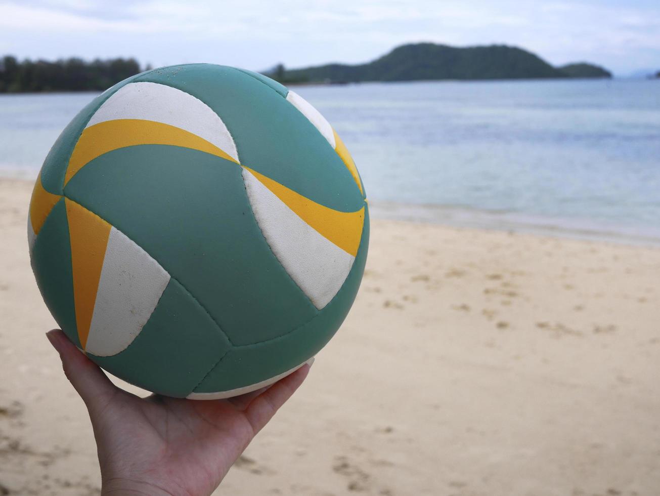 una mano che tiene il beach volley con sfondo spiaggia foto