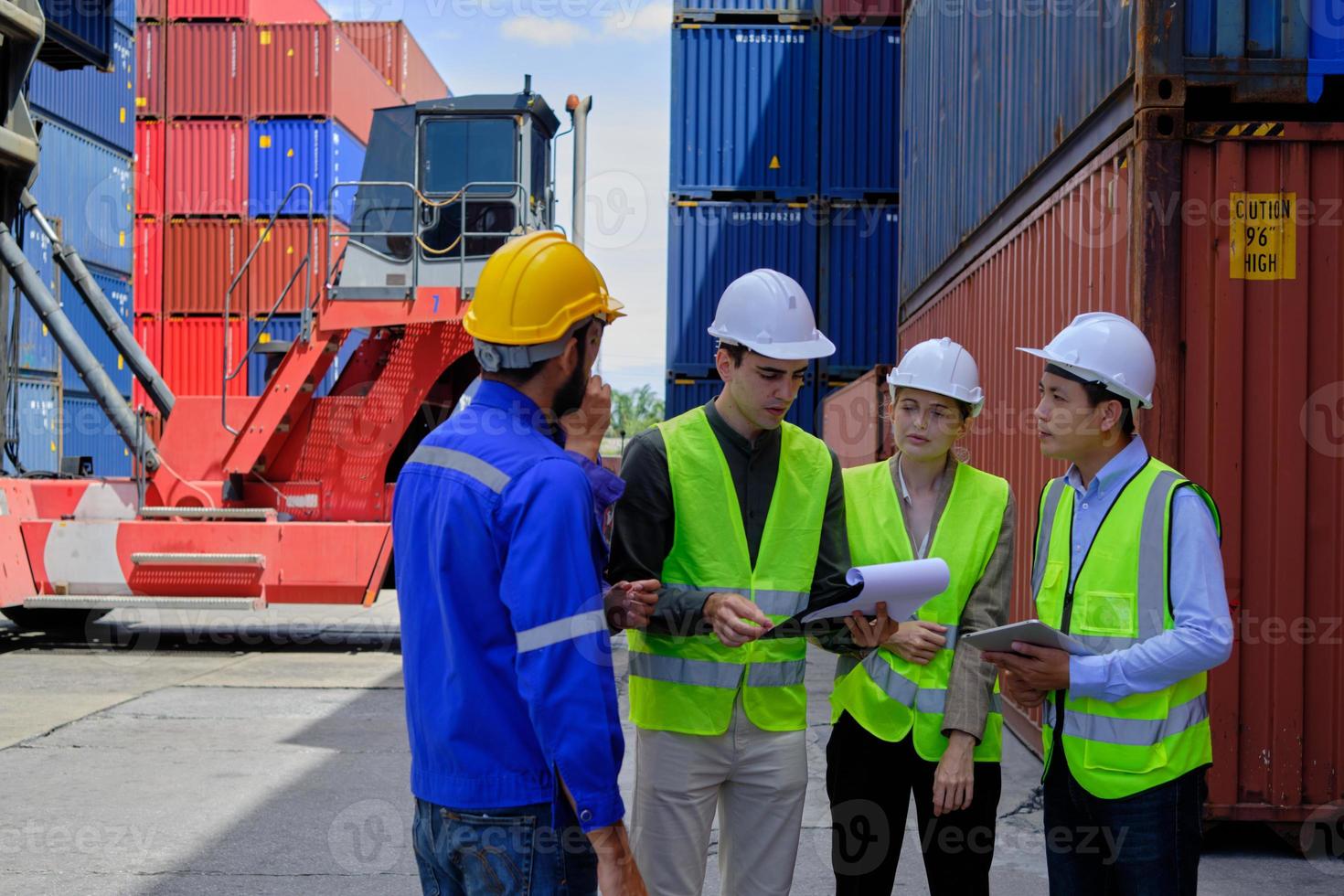 un gruppo di lavoratori multirazziali in divisa di sicurezza ed elmetti protettivi lavorano al terminal logistico con molte pile di container, caricando merci di spedizione controllate per l'industria del trasporto merci. foto