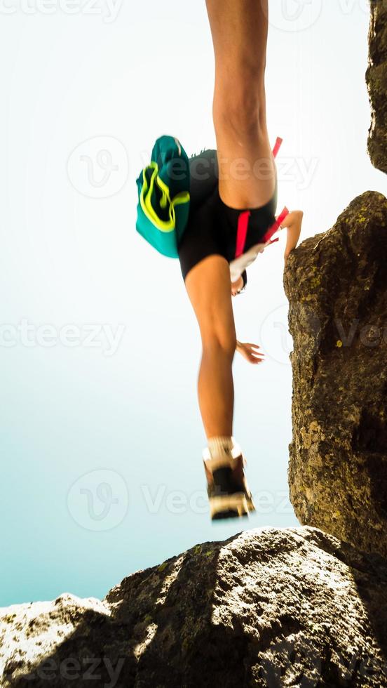 piedi di passo del corpo femminile di bassa vista in aria durante le escursioni sulle rocce all'aperto da soli in una calda giornata di sole all'aperto. filtro sfocatura movimento. impugnatura per scarpe e calzature concetto di arrampicata su roccia foto