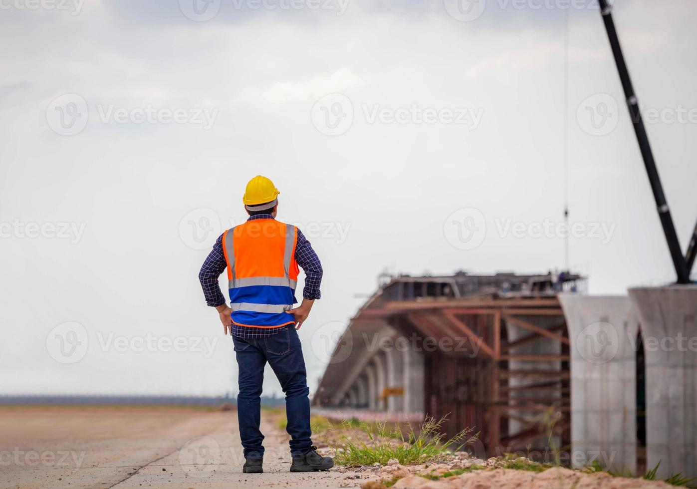 vista posteriore dell'ingegnere edile che controlla il progetto in cantiere, caposquadra in elmetto protettivo presso il cantiere dell'infrastruttura foto