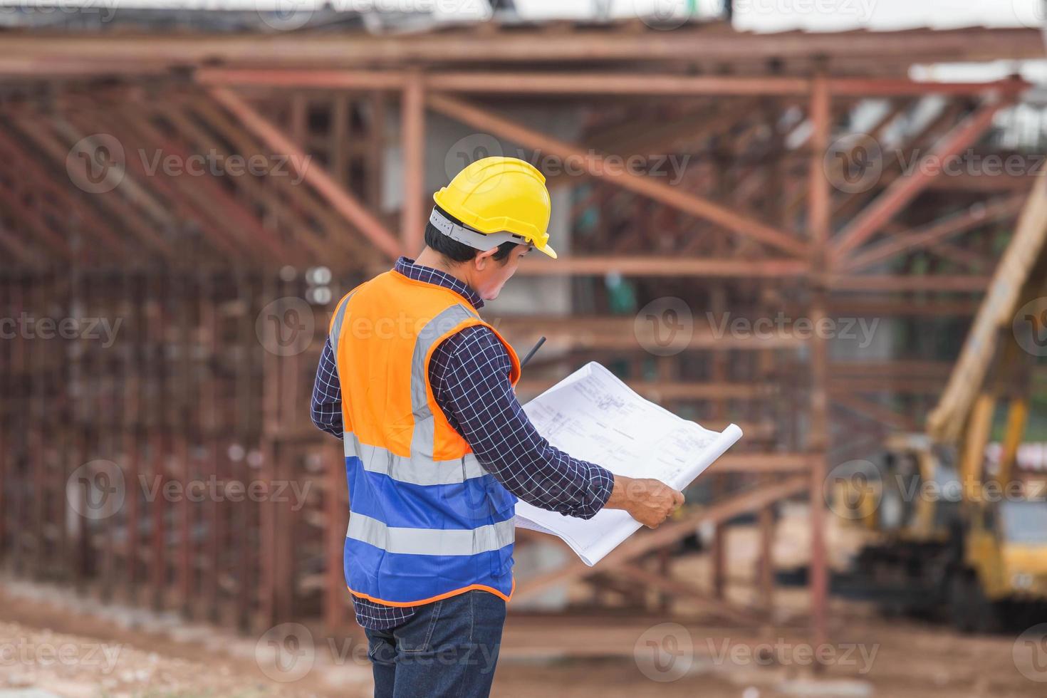 ingegnere edile asiatico che controlla il progetto in cantiere, architetto con progetti in un cantiere edile, caposquadra in elmetto protettivo presso il cantiere dell'infrastruttura foto