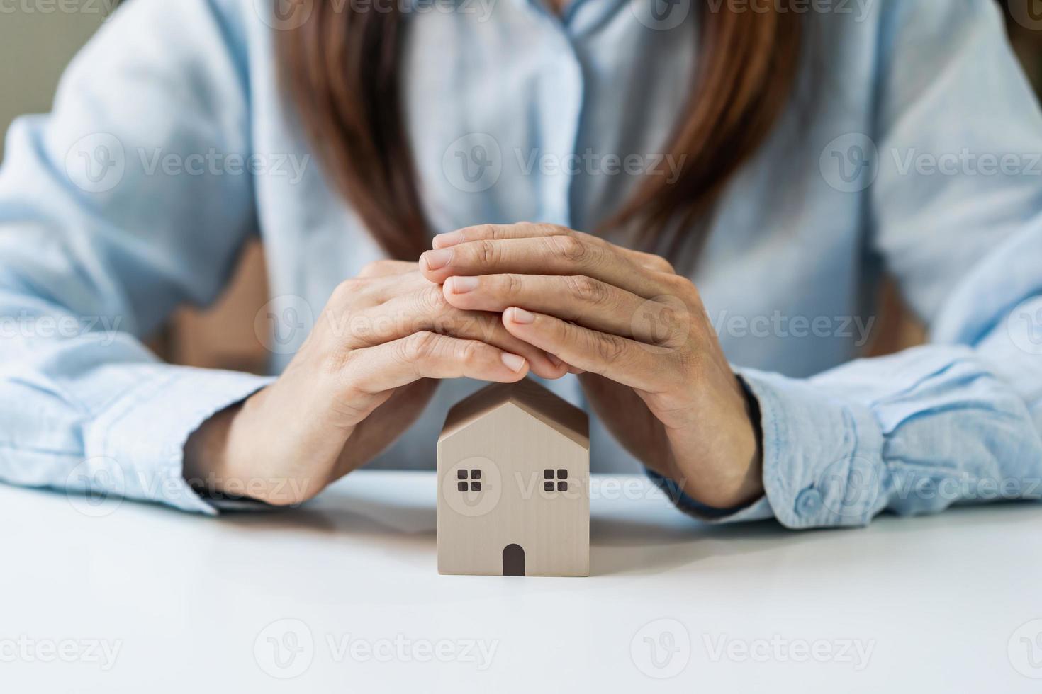 mani della giovane donna che proteggono la casa in miniatura, concetto di assicurazione sulla casa foto