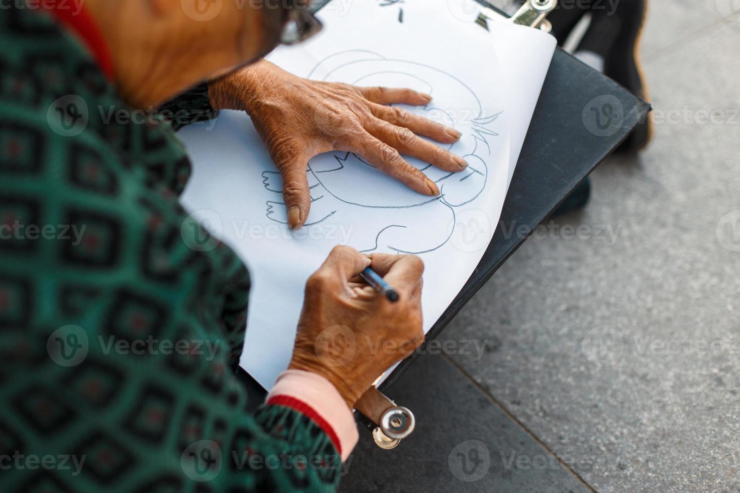 donna anziana con gli occhiali sta disegnando su carta. mano che tiene una matita foto