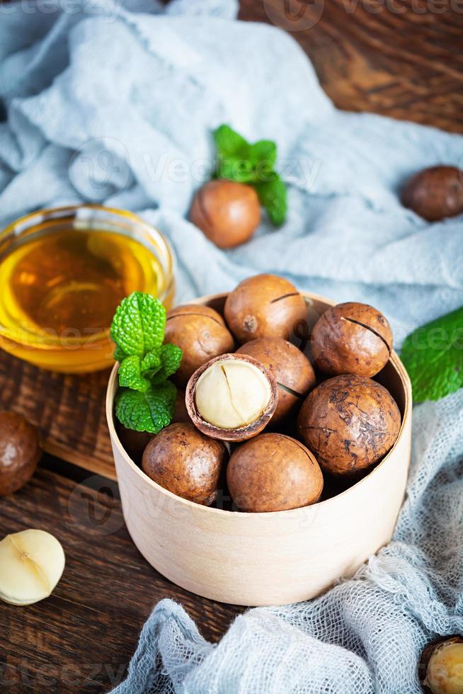 noci di macadamia in guscio con foglie di menta e miele su fondo di legno foto