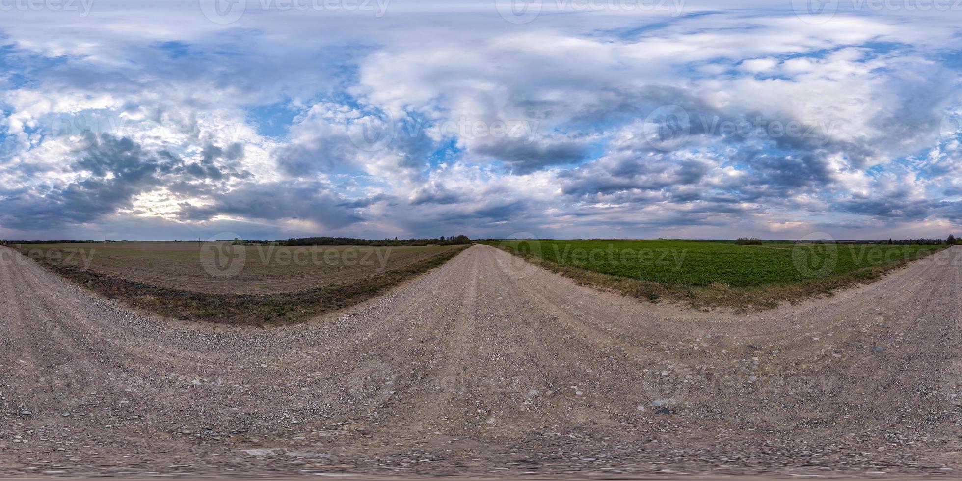 panorama hdri sferico completo e senza soluzione di continuità vista a 360 gradi su strada sterrata tra i campi in una giornata primaverile con nuvole temporalesche prima della pioggia in proiezione equirettangolare, pronto per contenuti vr ar foto