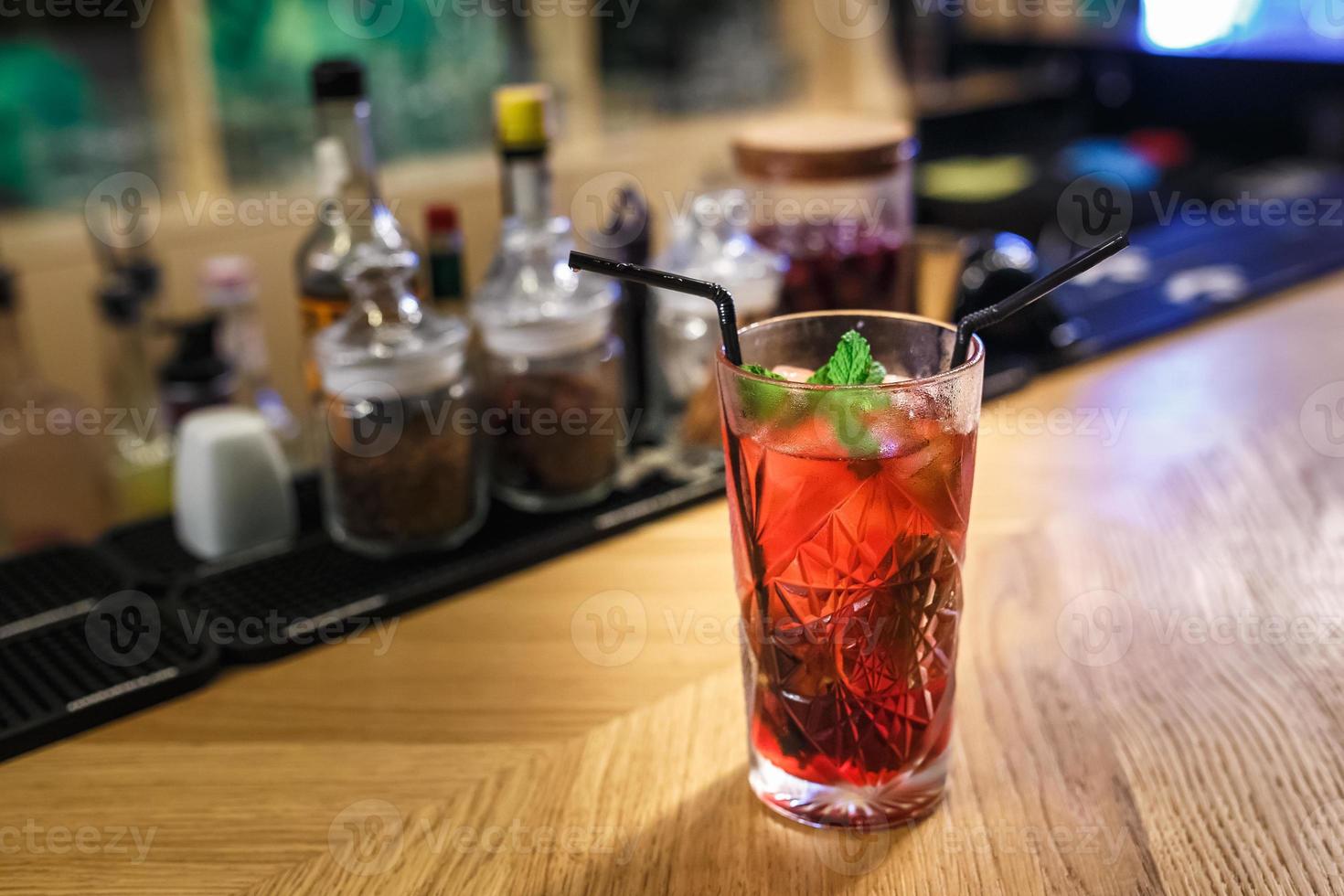 cocktail rosso in un bicchiere con menta e due tubi su un tavolo in un bar di lusso foto