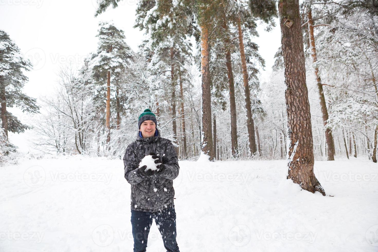 un giovane con una palla di neve in mano si diverte, dondolandosi per un tiro. inverno in famiglia e simpatici giochi e divertimenti nel bosco con neve all'aria aperta foto