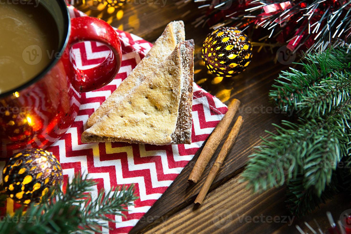 biscotti triangolari con zucchero a velo e cannella su un tovagliolo con motivo a zigzag nell'arredamento natalizio. tazza da caffè rossa con marshmallow, rami di abete, ghirlanda, capodanno, comfort. foto