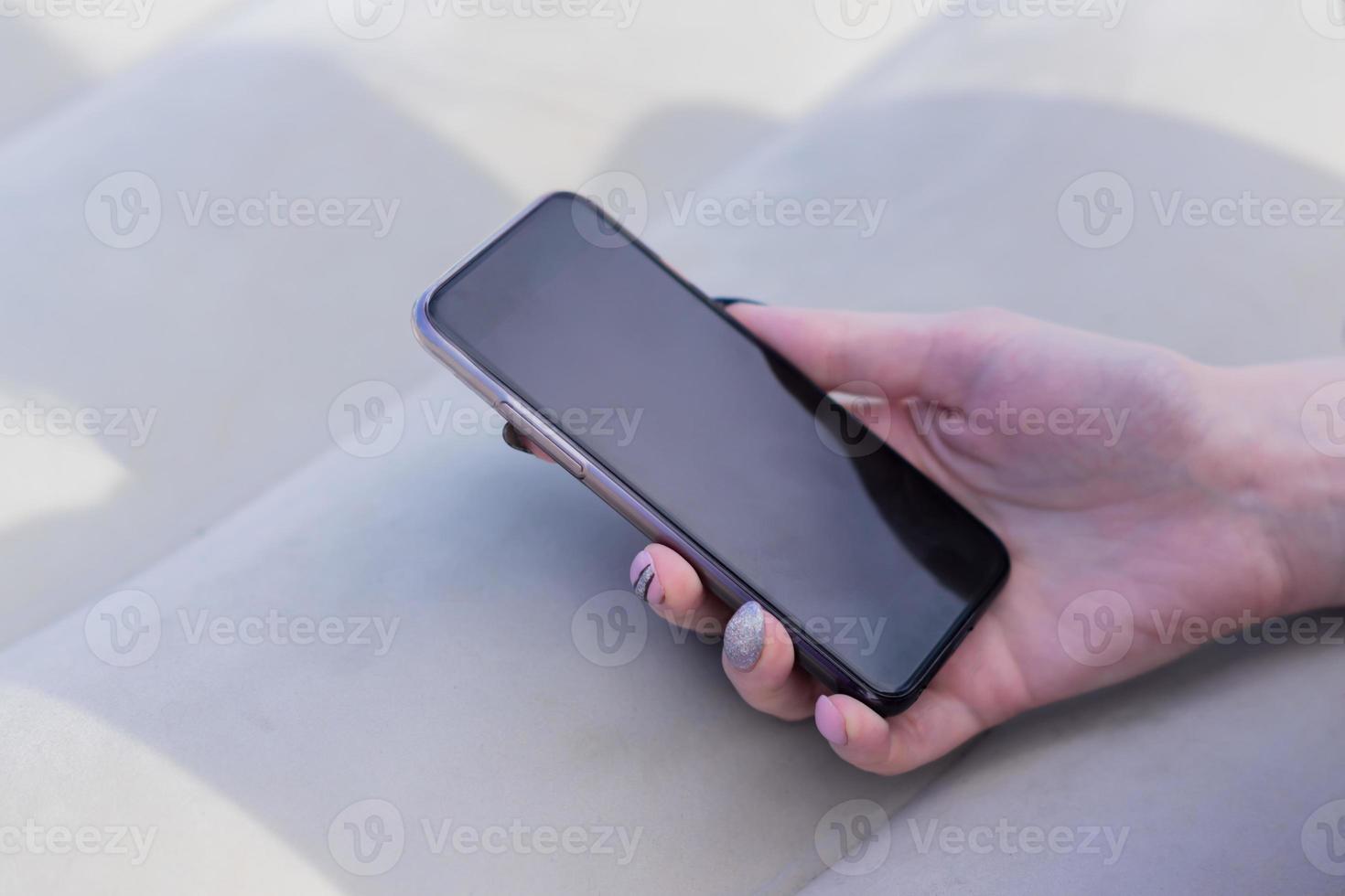 mano femminile con manicure che tiene smartphone nero foto